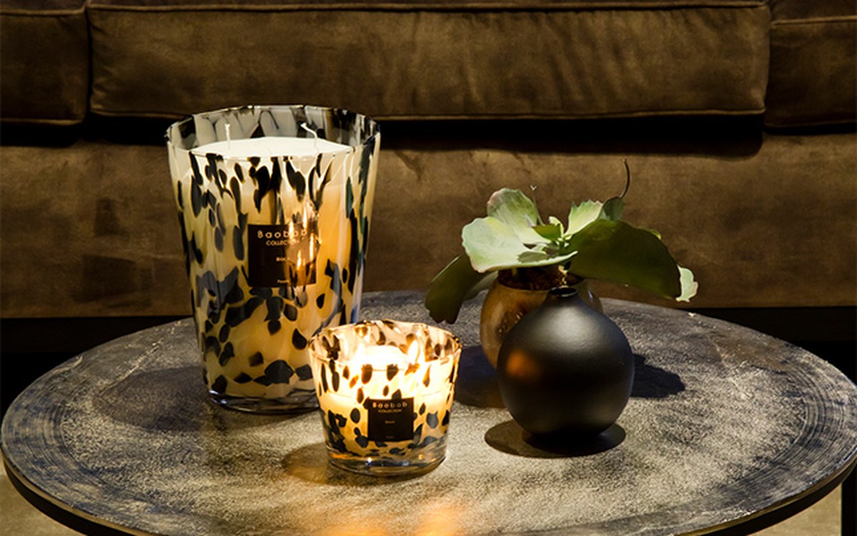 Two hand-blown Baobab Collection candles in leopard-print glass, sat on a round table in the Corbridge snug beside a black ceramic vase