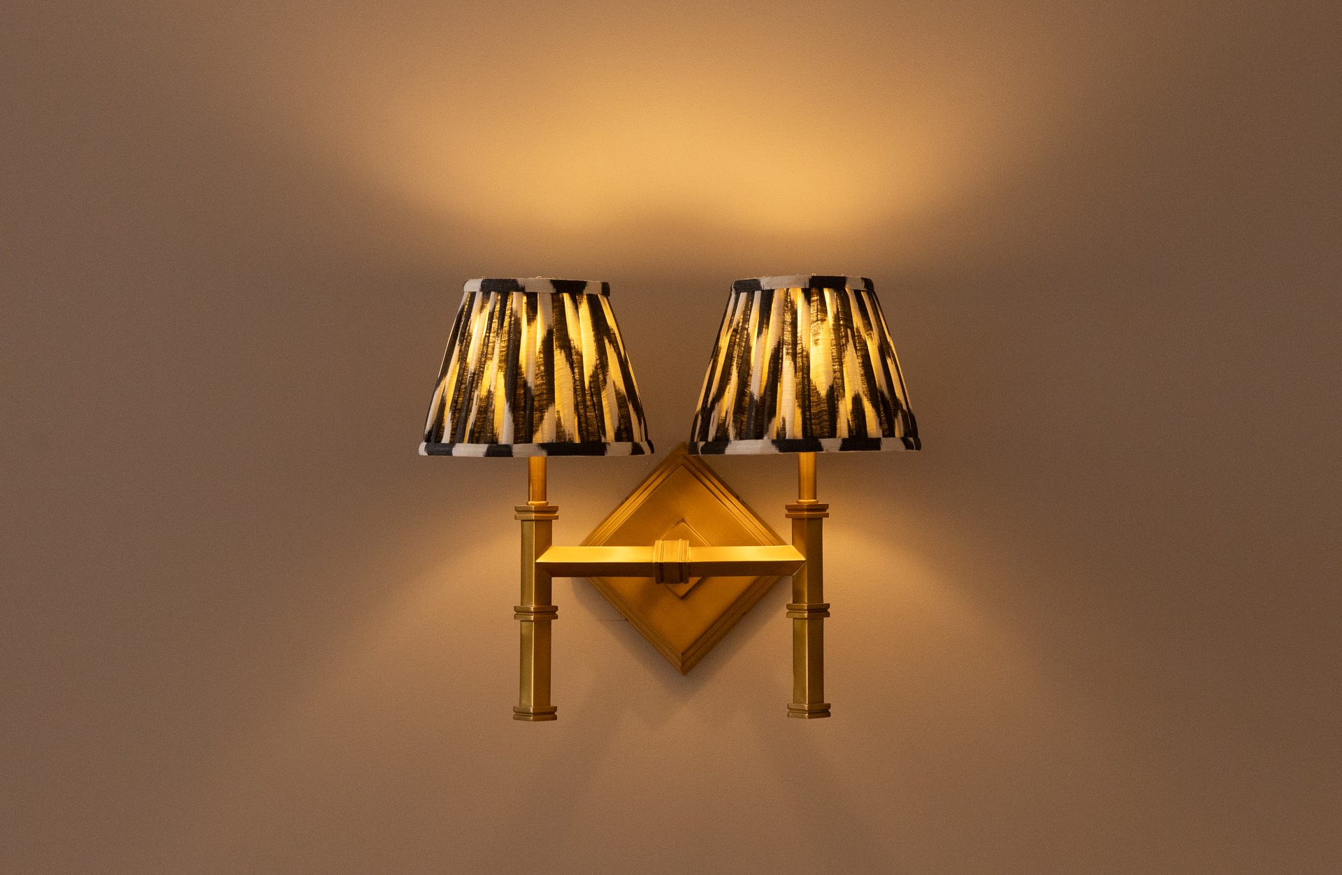 Brass ribbon sconce lit on a warm taupe wall