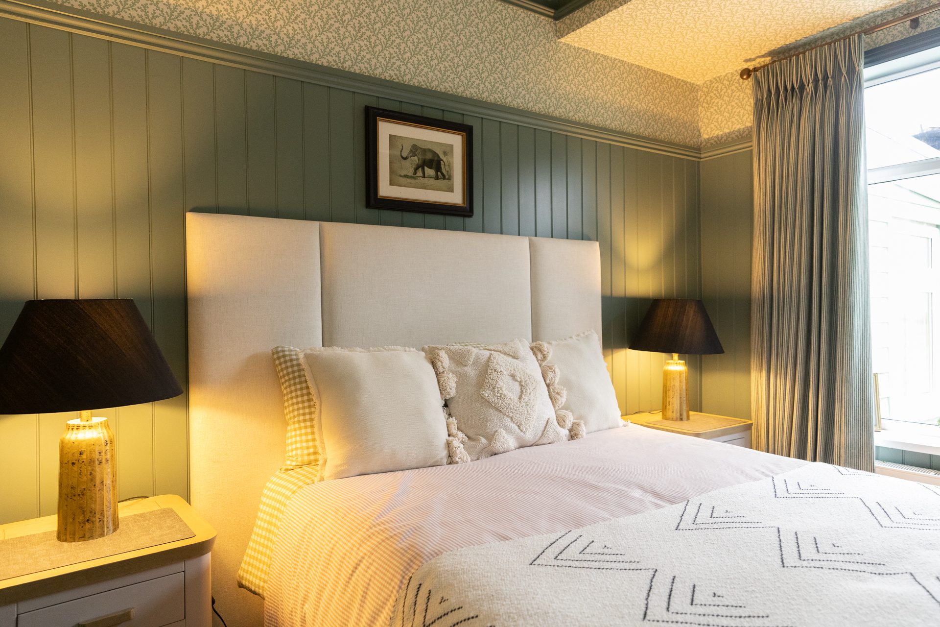 The Bamburgh master bedroom, sage panelling taken to picture-rail height with a deep upholstered bed in white cotton