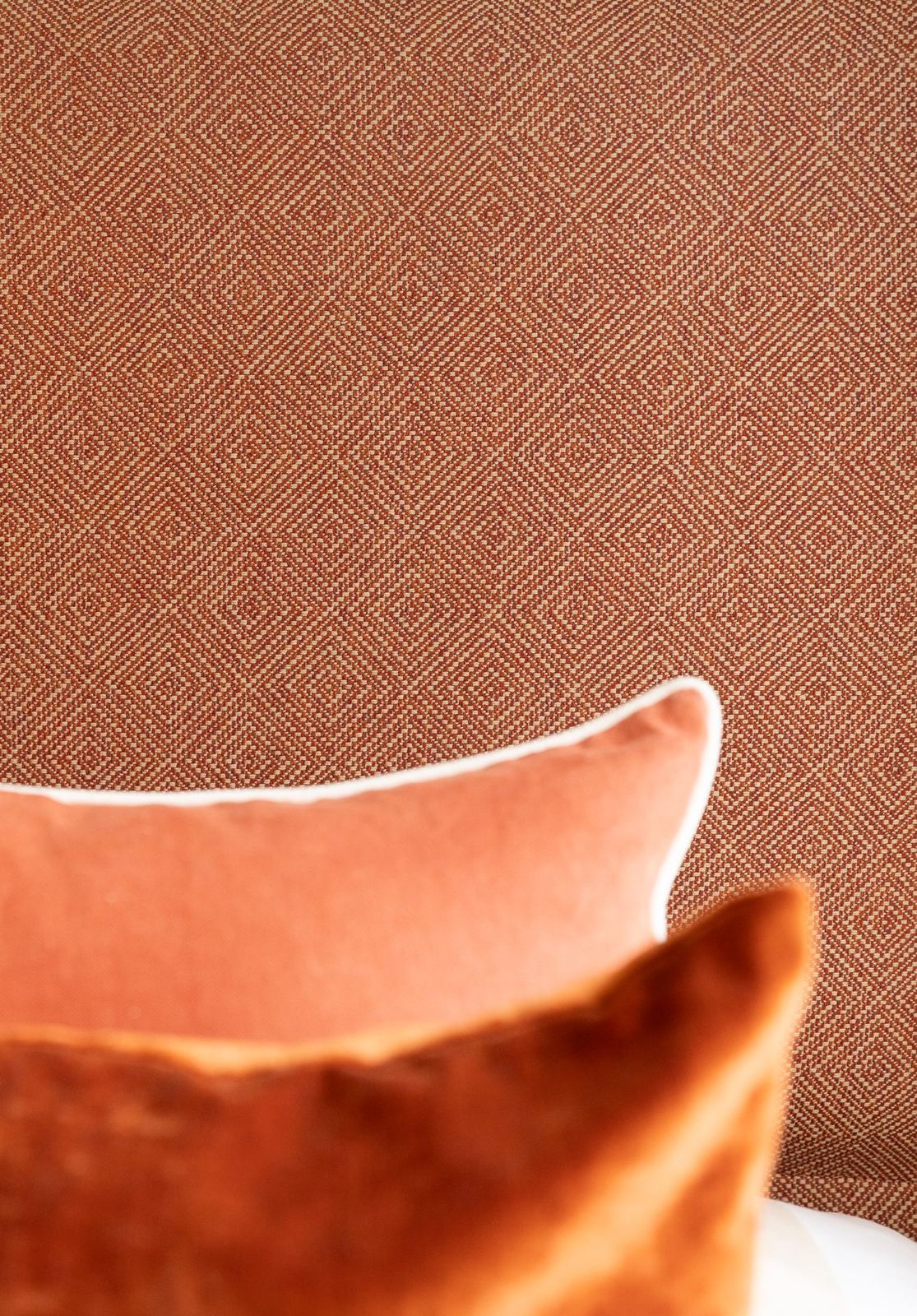 Close detail of the woven mushroom-and-cream diamond pattern on the headboard fabric, rust velvet cushion in foreground