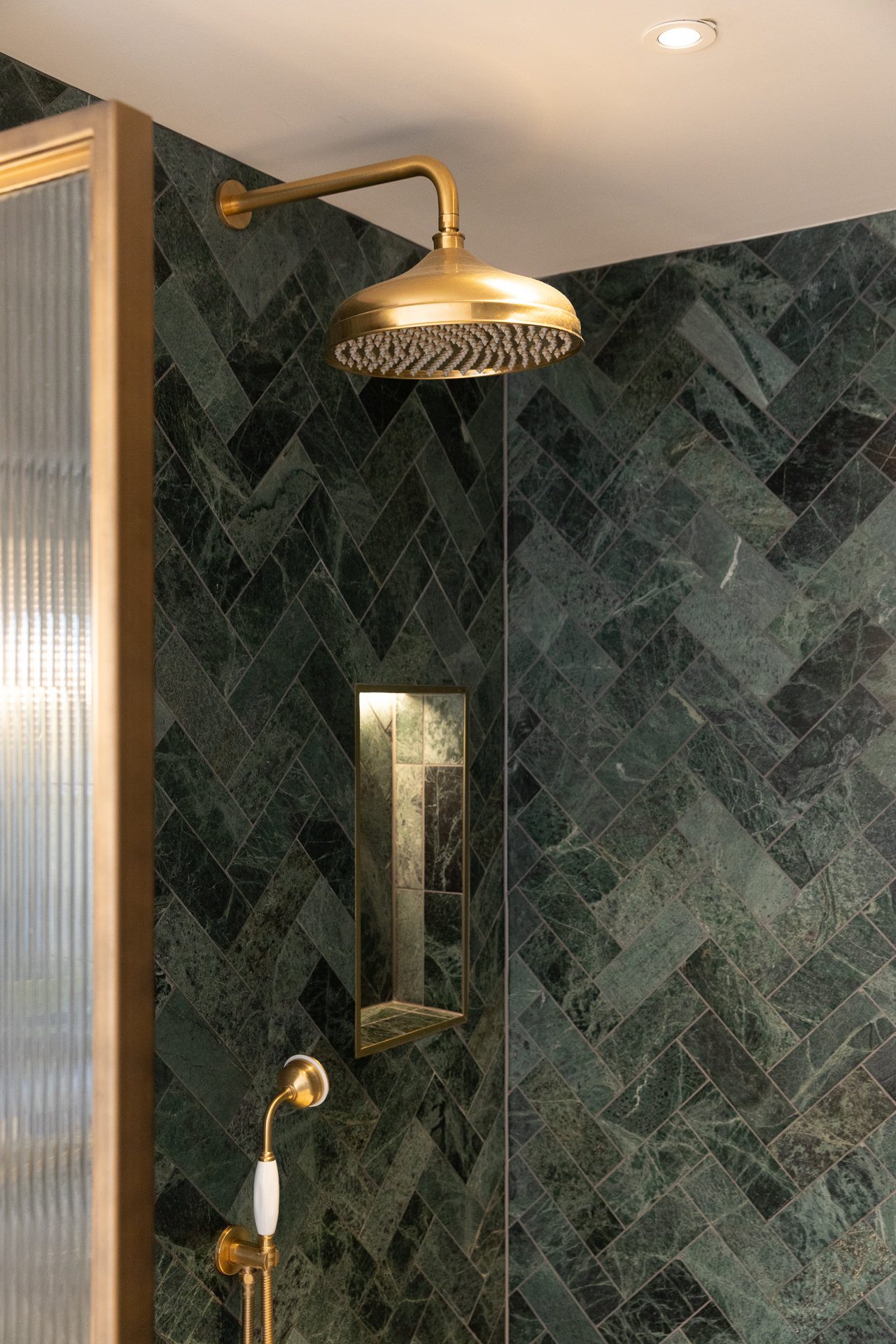 Herringbone green marble shower wall at Elmfield Road with a large brass rain head on a wall-mounted brass arm and a slender recessed niche