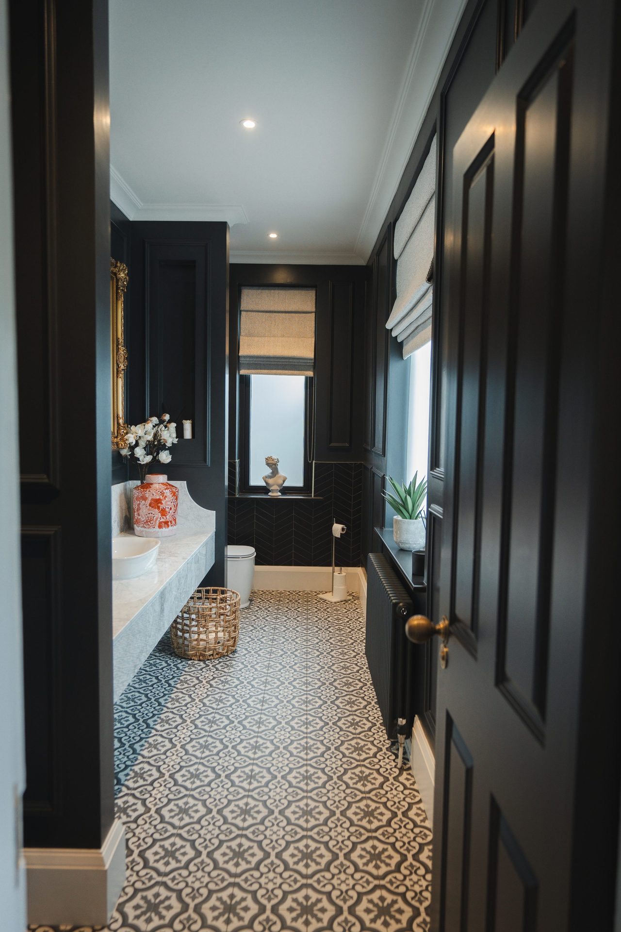 View into the Montagu WC through the panelled door, navy joinery, marble vanity with vessel basin, patterned floor tile and a gilt-framed mirror