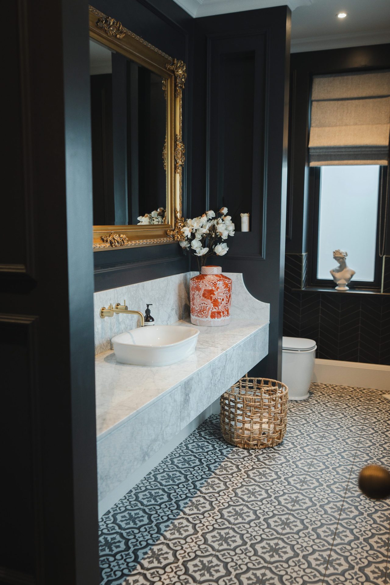 Montagu project, black panelled bathroom with marble vanity, ornate gilded mirror, chandelier overhead and geometric patterned tile floor