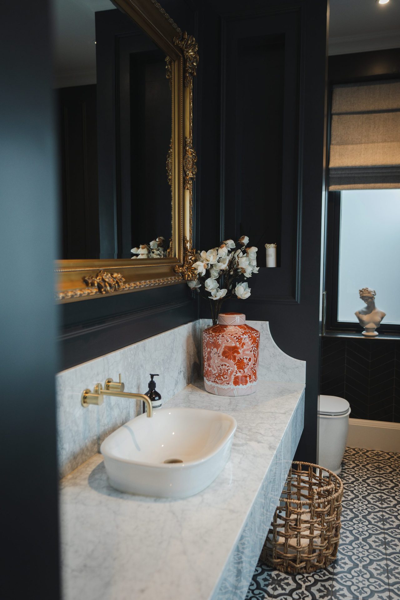 The ornate gilded mirror above the marble vanity in the W.C, seen in portrait, with black panelled walls rising behind