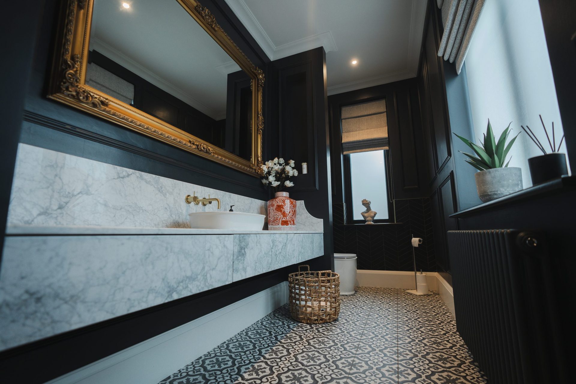 Montagu bathroom vanity held straight-on, ornate gilded mirror above a marble floating vanity with chrome taps and a small pink patterned lamp