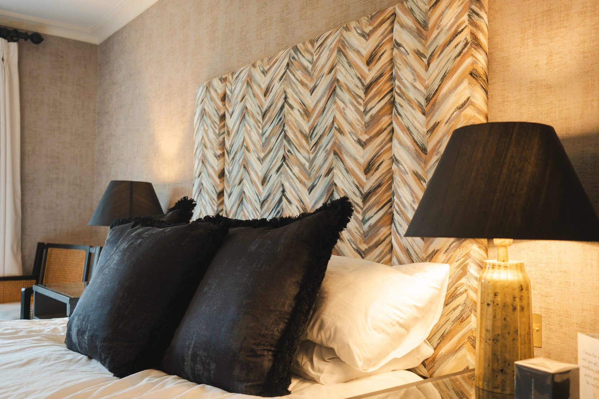The Montagu bedroom, textured chevron headboard, black and cream pillows, a gold lamp warming the bedside