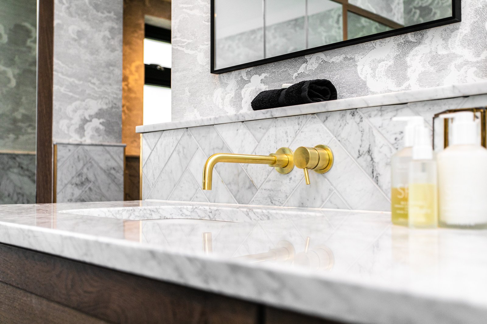 Close detail of brass cross-handle taps above a fluted basin, marble splashback beyond