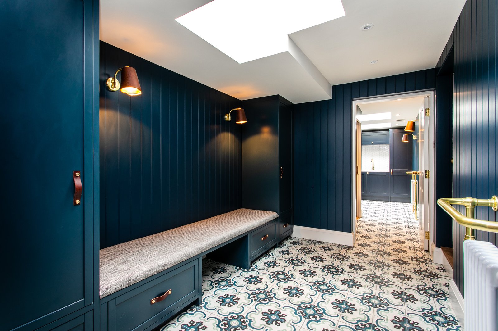 A navy panelled bench in the boot room, open storage below, a patterned encaustic tile in blues and greens carried across the floor
