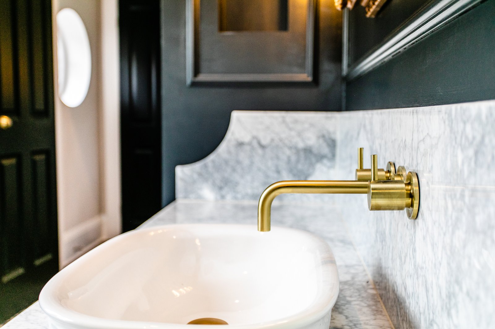 An unlacquered brass wall-mounted bath tap and hand-held shower, set against honed marble