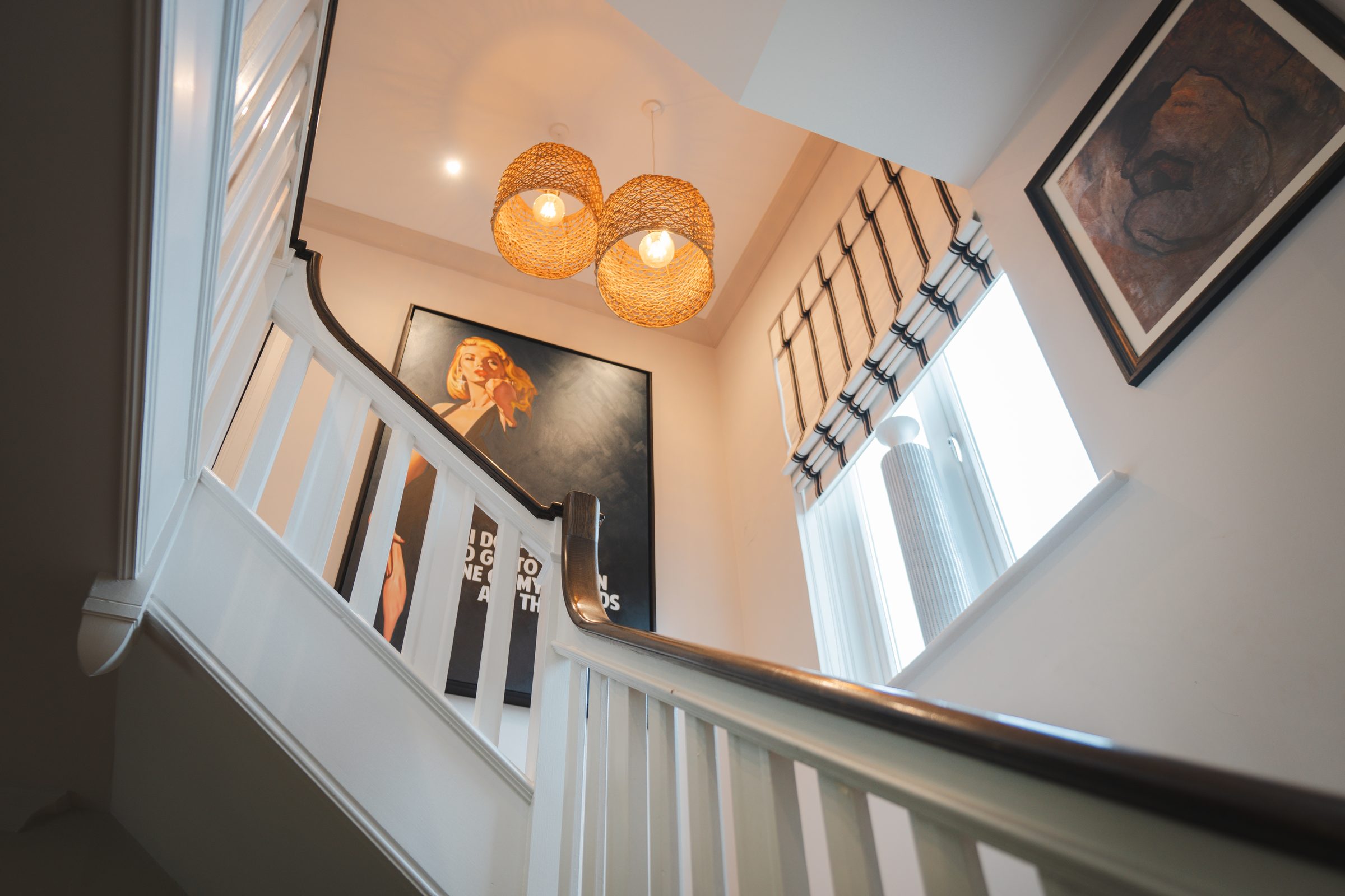 Looking down the Montagu staircase from the landing, twin rattan pendants hanging low, a framed black-and-white portrait at the turn