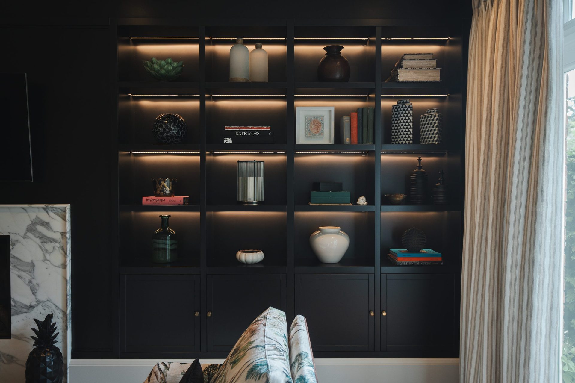 A full wall of dark built-in shelves, each bay lit from inside, staging vases, books and ceramics