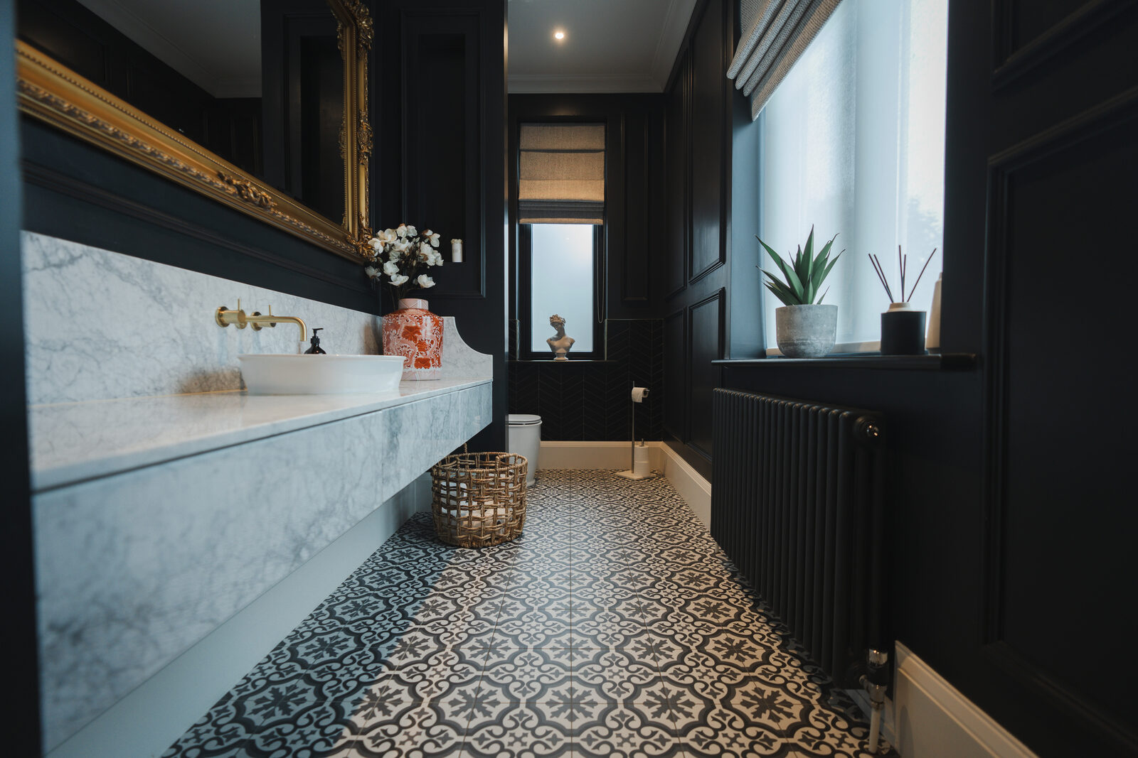 The Montagu W.C, black panelled walls, a floating marble vanity, brass fittings and a geometric patterned tile floor running the length of the room
