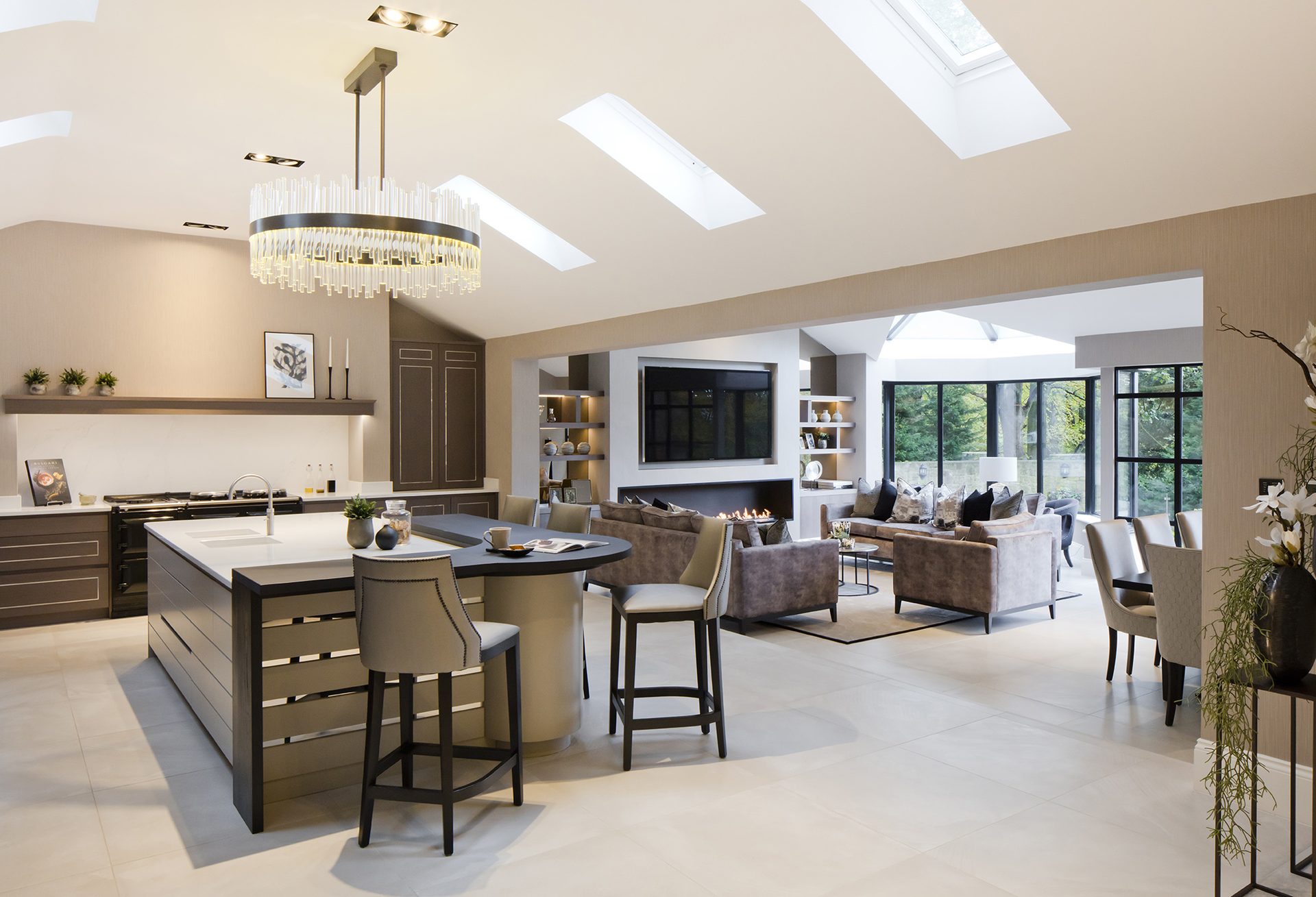 Open plan kitchen at The Northumberland Project — island with bar stools, crystal chandelier, skylights, living and dining beyond