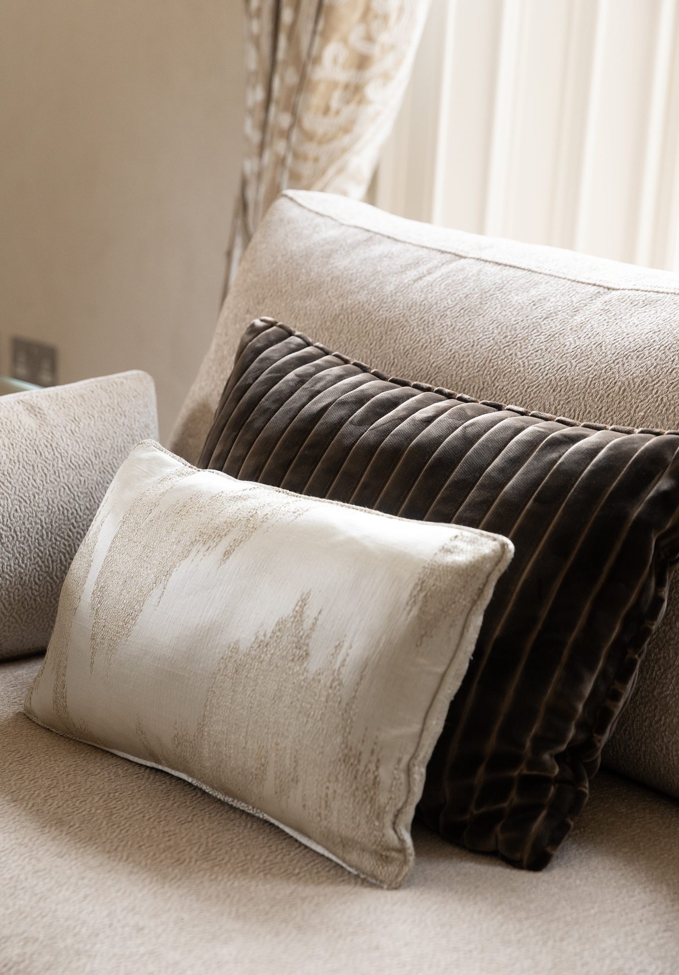 Three cushions in close detail, a cream texture, a pleated dark-brown velvet, an ivory accent