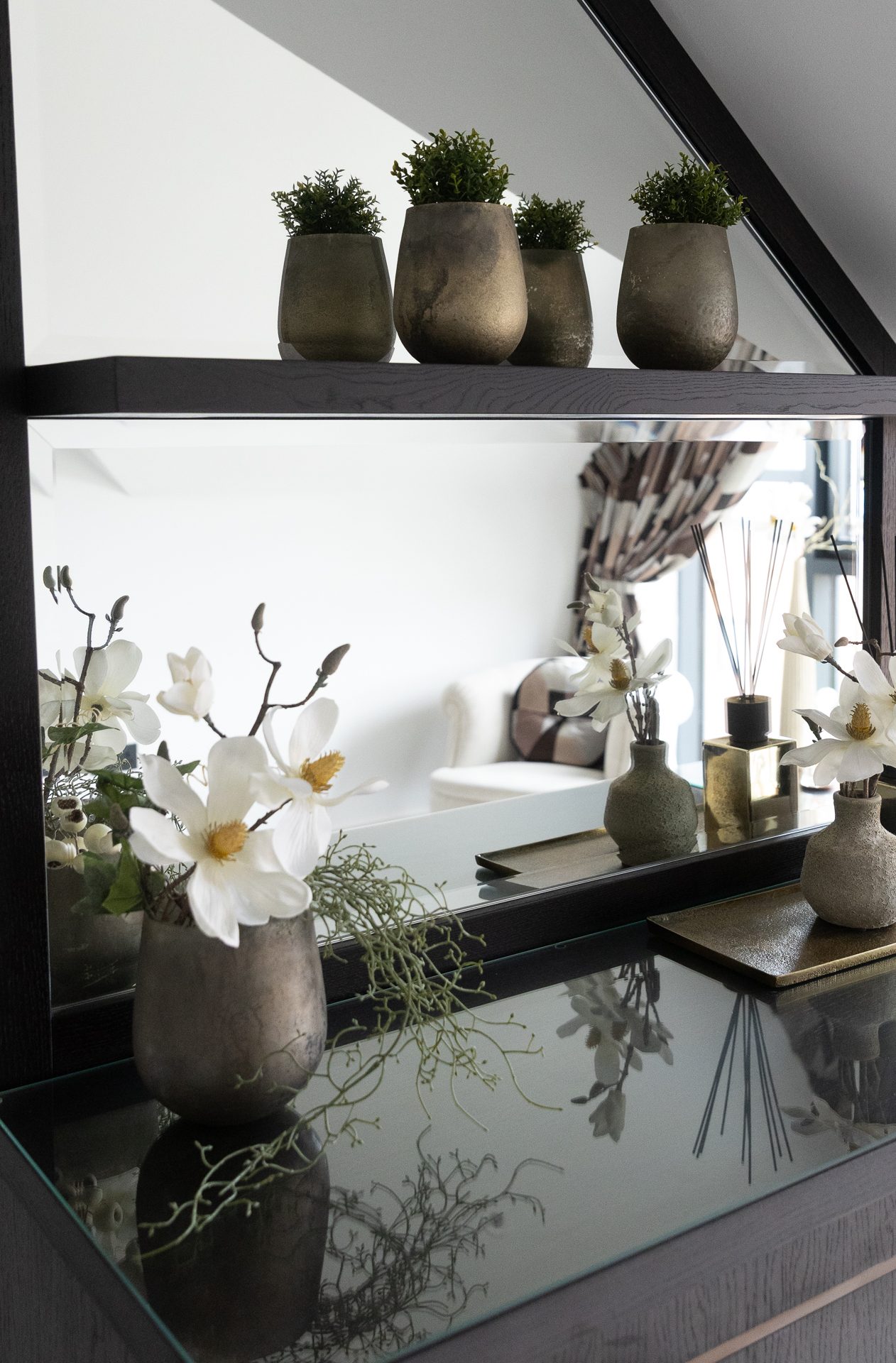 Dark mirrored dressing unit cut to the sloped eaves, pewter pots of greenery above and magnolias below
