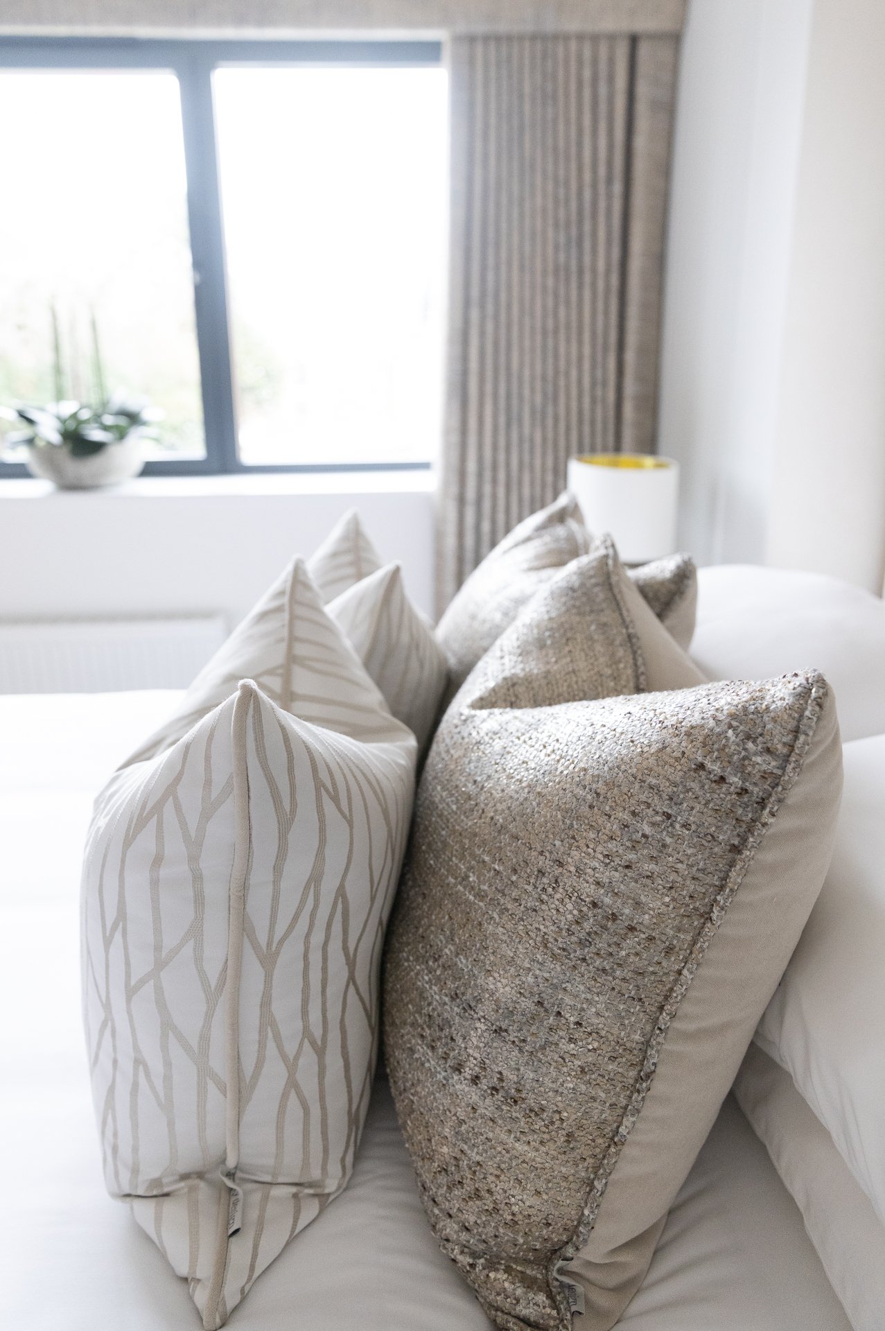 Two pillows with tonal linen-and-silver weave propped against a cream headboard
