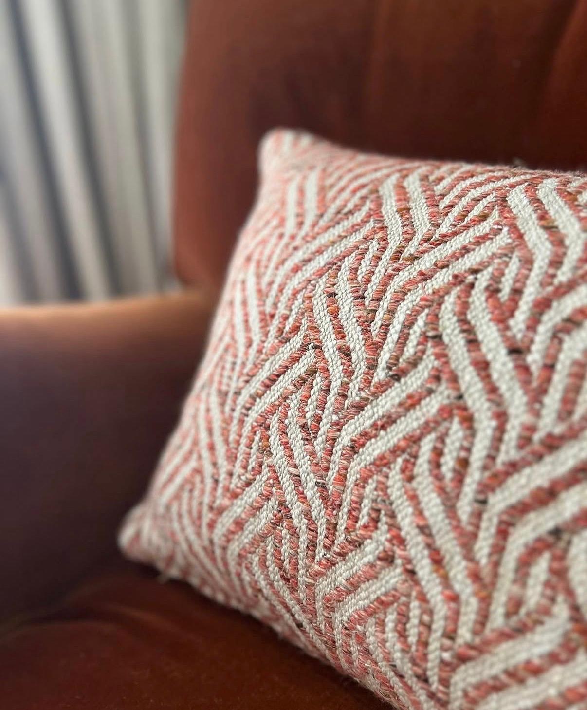 A coral pink and cream herringbone-pattern cushion on a rust leather chair, with blue stripe blinds behind — Christopher Farr Cloth's hand-printed artisan fabric in an Aubury room