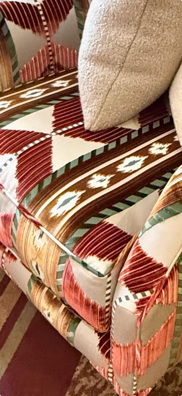 Detail of an upholstered chair in multi-coloured chevron and aztec velvet pattern, paired with a cream boucle cushion — a recent Aubury fabric choice from Osborne & Little