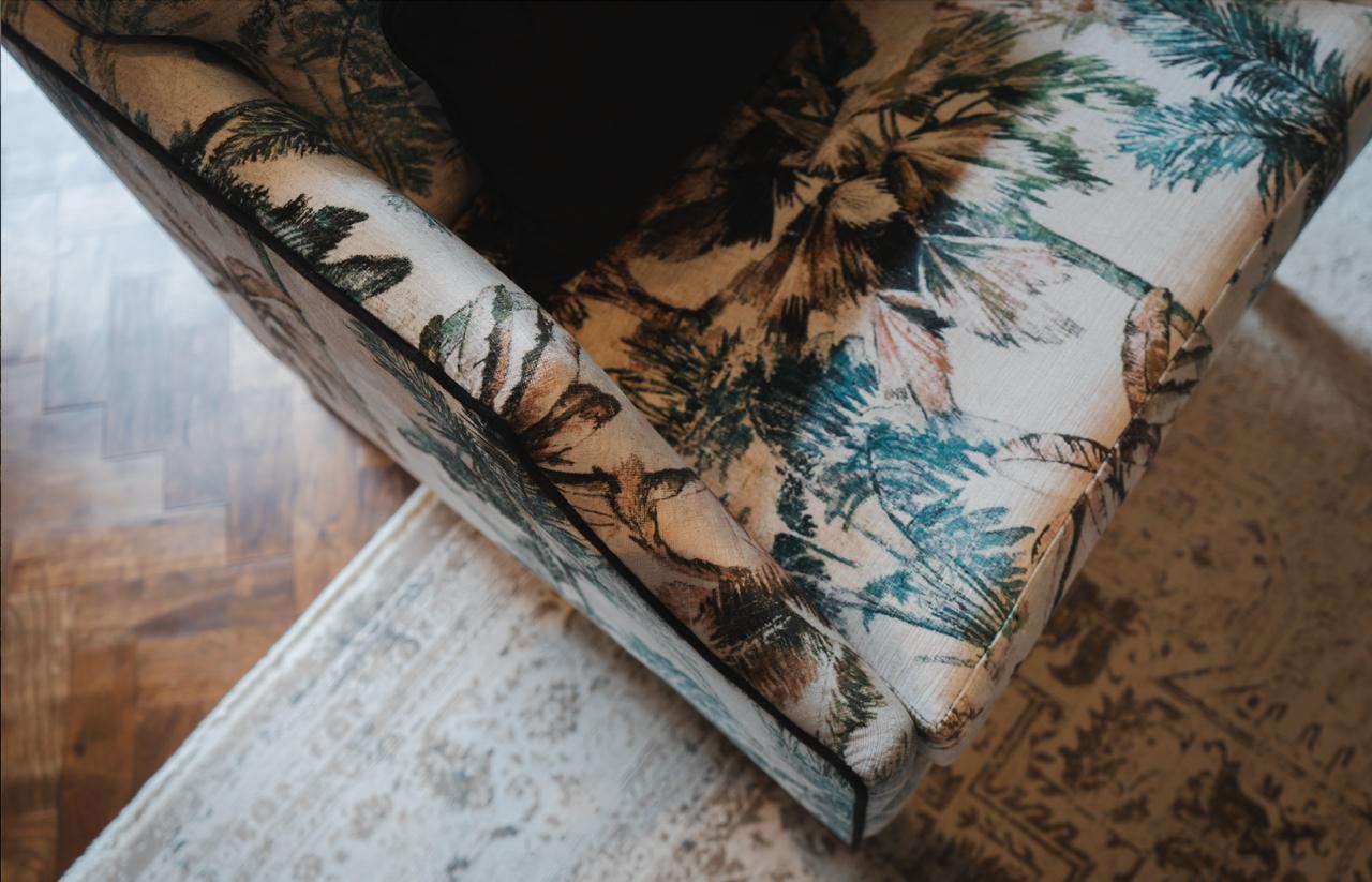 A tropical palm-print upholstered chair on dark parquet over a cream rug, the kind of confident pattern Romo bring to a scheme